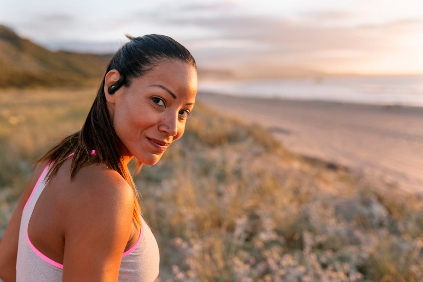 JBL apresenta novo fone esportivo, o JBL Endurance Peak 4 1 Portrait of a beautiful smiling woman on the beach at sunset. She looks directly into the camera